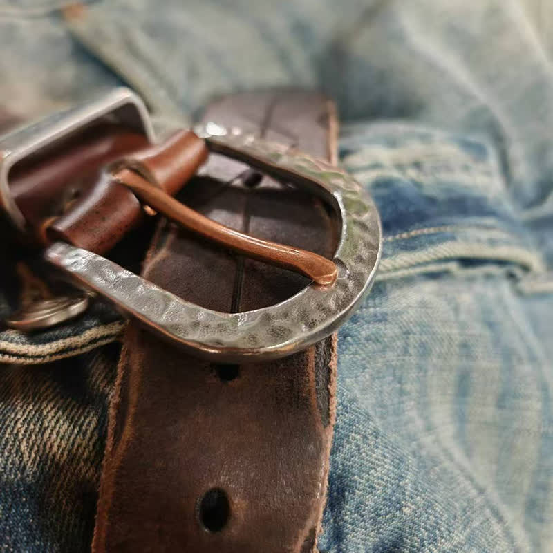 Cinturón de cuero con diseño de flecha tallada y hebilla de martillo de plata.