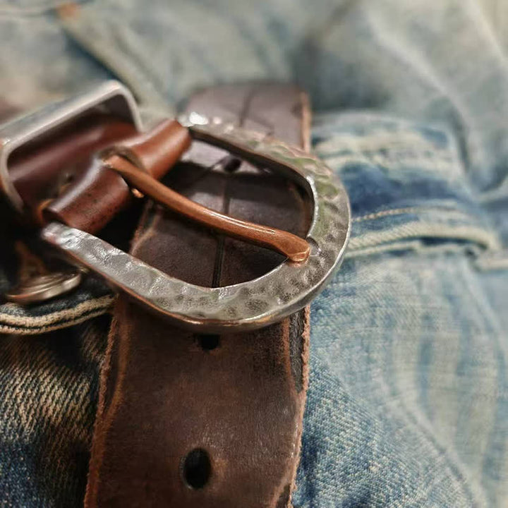 Cinturón de cuero con diseño de flecha tallada y hebilla de martillo de plata.