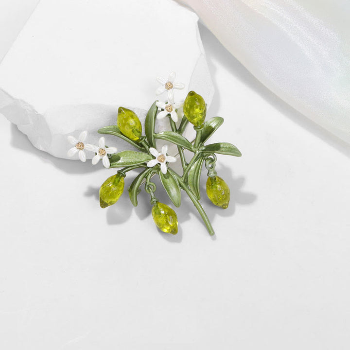 Broche de mujer con forma de gota de limón y planta verde.