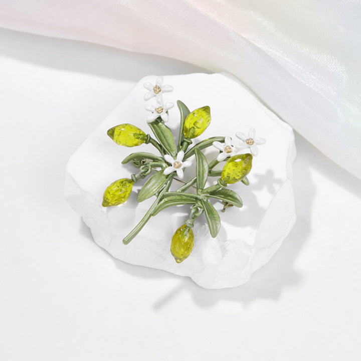 Broche de mujer con forma de gota de limón y planta verde.